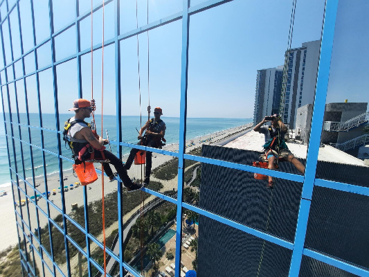 Two Window Ninjas Charleston team members cleaning the windows outside a high-rise commercial building.