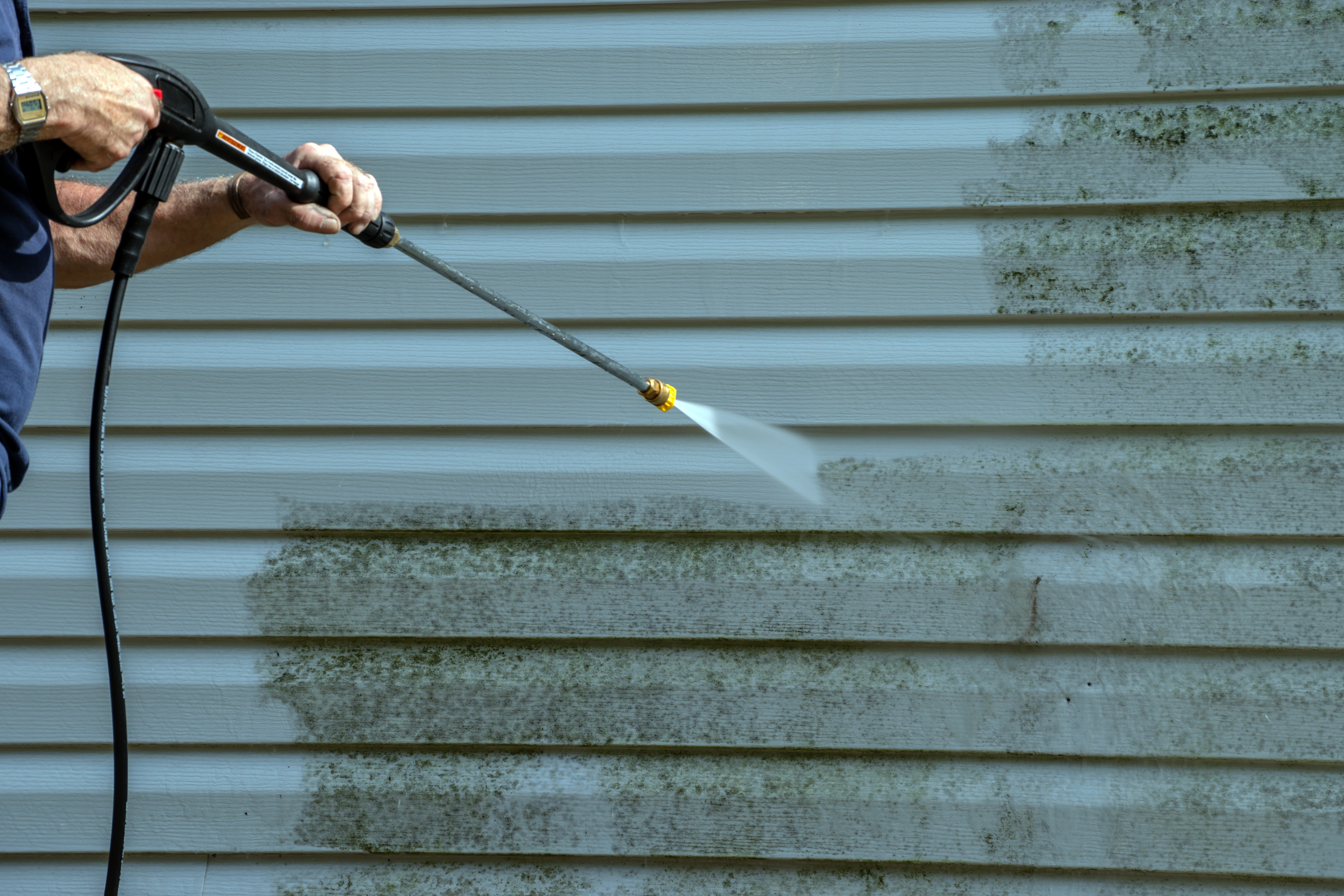 A technician using a pressure washer to remove dirt and grime from the outside of a building. 