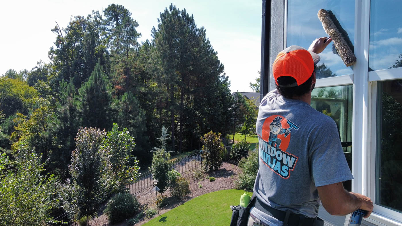 A Window Ninjas Greenville / Spartanburg washing expert cleaning the outside windows for a tall residential home.